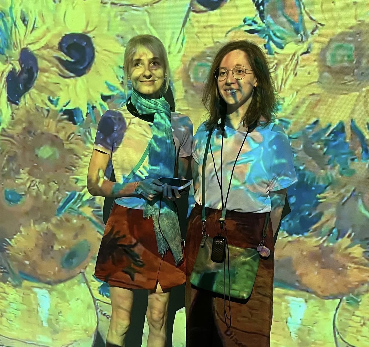 Two people smiling in front of a wall-sized projected sunflowers painting